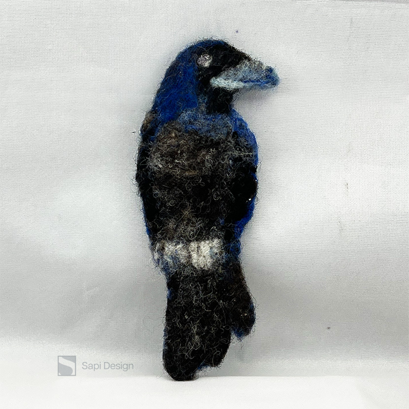 Käsin lampaanvillasta huovutettu kolmiulotteinen korppi rintakoru.